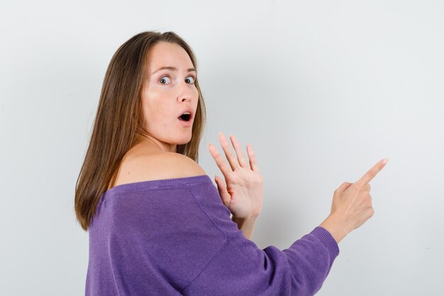 Young female showing no gesture and pointing away in violet shirt and looking scared. .