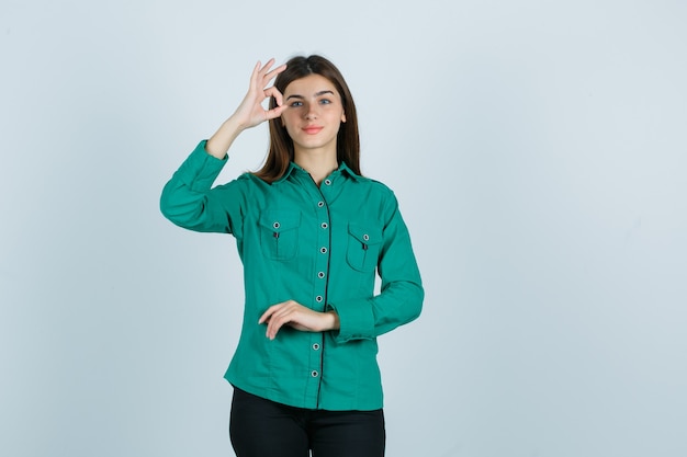 Young female showing ok gesture in green shirt and looking cheery , front view.