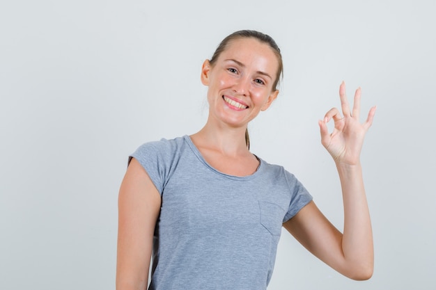 Молодая женщина показывает нормально жест в серой футболке и выглядит довольной. передний план.