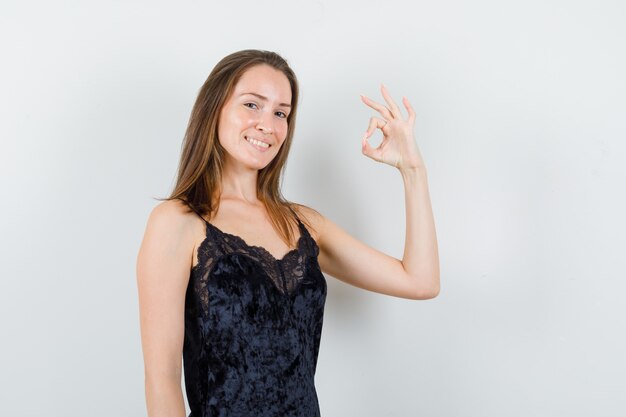 Young female showing ok sign in black singlet and looking cheerful