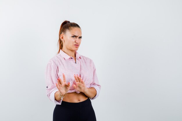 Young female showing palms in surrender gesture in casual shirt and looking displeased , front view.