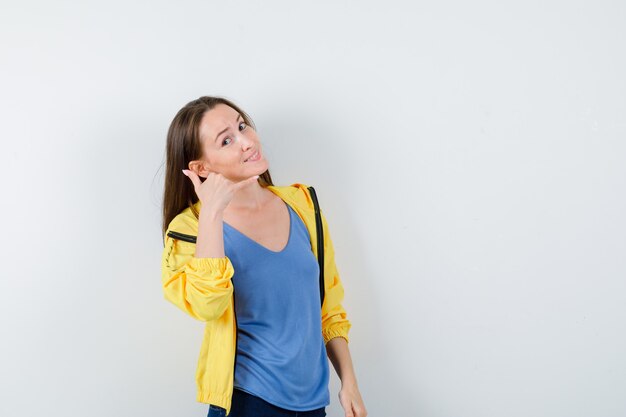 Young female showing phone gesture in t-shirt and looking confident, front view.