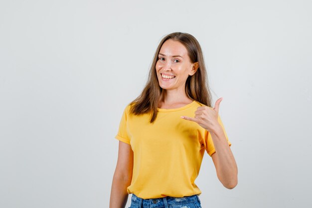 Молодая женщина показывает жест телефона в футболке, шортах и выглядит веселой