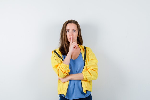 Young female showing silence gesture in t-shirt, jacket and looking careful , front view.