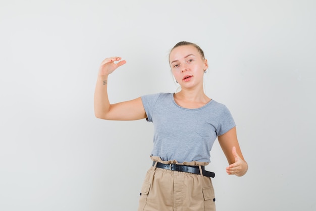 Бесплатное фото Молодая женщина показывает знак размера в футболке, вид спереди брюки.