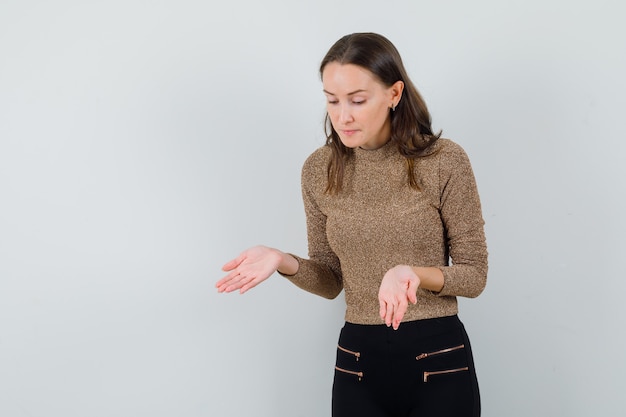 金色のブラウスで開いた手のひらで床に何かを見せて、真剣に見える若い女性。正面図。