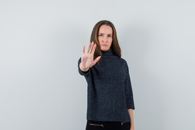 Young female showing stop gesture in black blouse and looking serious. front view.