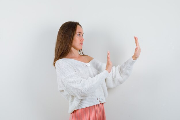 Молодая женщина показывает жест остановки в кардигане и юбке, выглядит испуганной изолированной