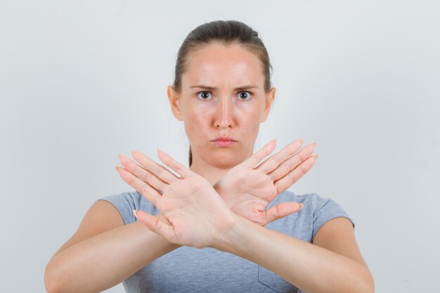 Young female showing stop gesture in grey t-shirt and looking serious. front view.