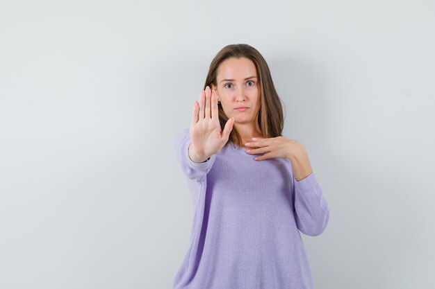 Young female showing stop gesture in lilac blouse and looking strict 