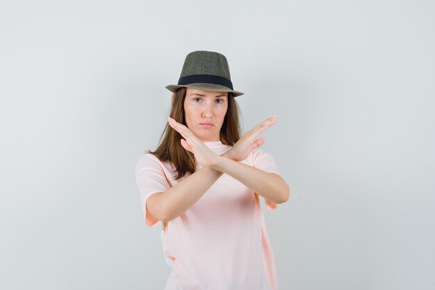 ピンクのTシャツ、帽子、真剣に見える、正面図で停止ジェスチャーを示す若い女性。
