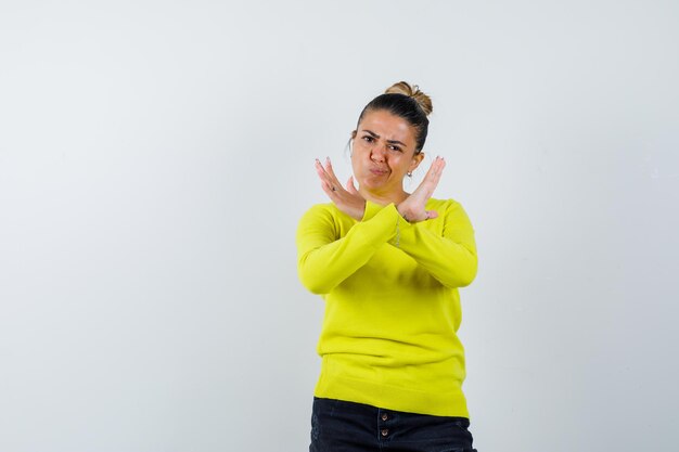 Young female showing stop gesture in sweater, denim skirt and looking confident 