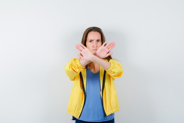 Young female showing stop gesture in t-shirt, jacket and looking resolute. front view.