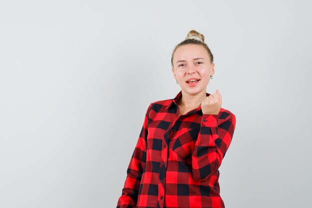 Young female showing success gesture in checked shirt and looking happy. front view.