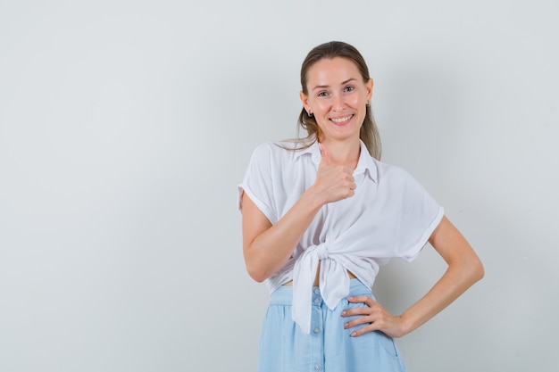 Young female showing thumb up in blouse and skirt and looking jovial