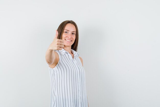 Молодая женщина показывает палец вверх в футболке и выглядит веселым, вид спереди.