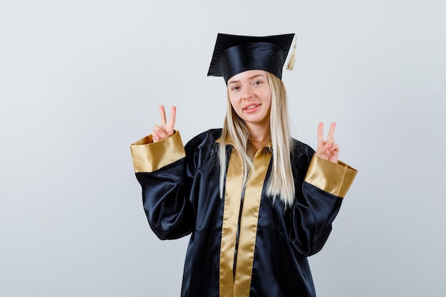 Молодая женщина показывает знак V в униформе выпускника и выглядит веселой