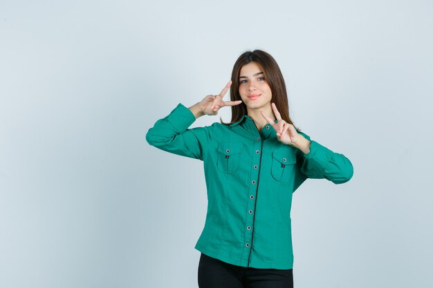 Young female showing victory gesture in green shirt and looking cheerful , front view.