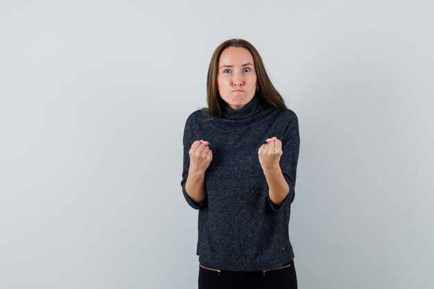 Young female showing winner gesture in black blouse and looking insistent. front view.