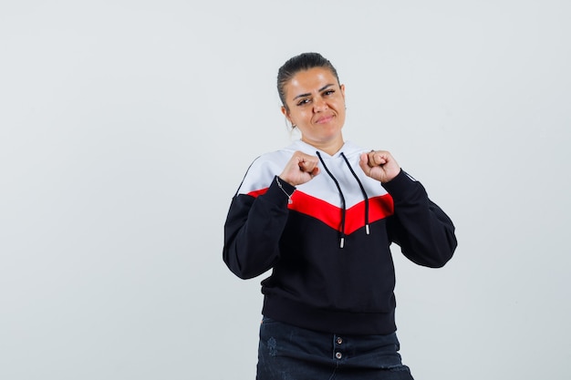 Young female showing winner gesture in colorful sweatshirt and looking glad. front view.
