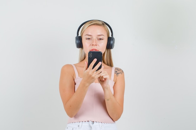 Young female in singlet, mini skirt, headphones talking on videocall 