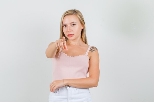 Young female in singlet, mini skirt pointing finger to camera 