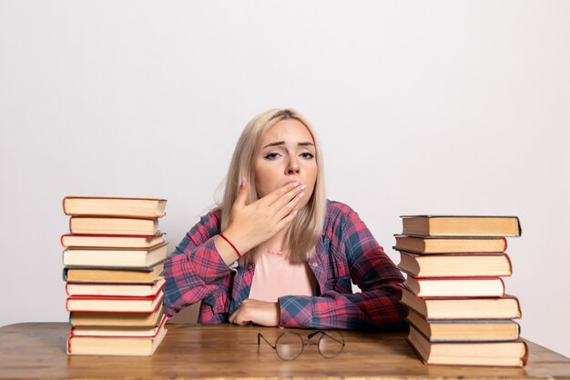 young female sitting with books feeling tired on white