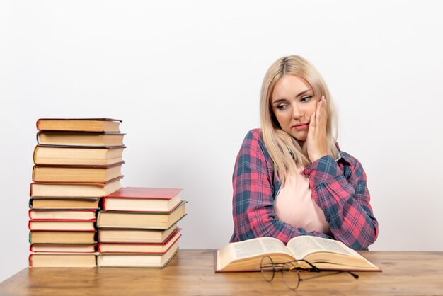 young female sitting with books and reading on white