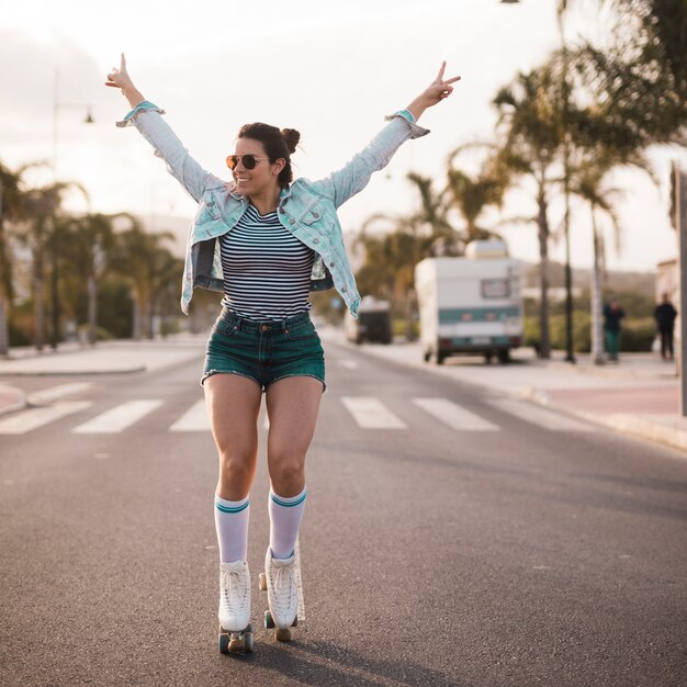 Young female skater raising her arms making peace gesture balancing on road