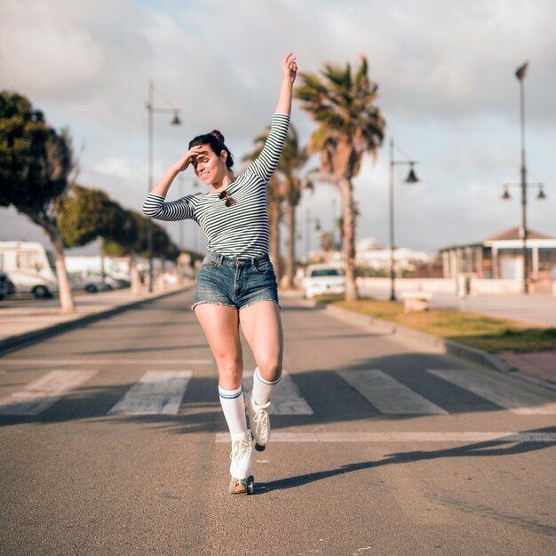 彼女の腕を持つ若い女性スケーターは道路上で踊りを調達