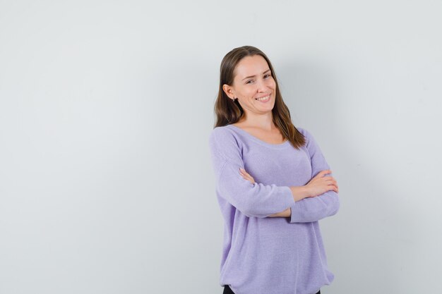 Young female smiling while keeping arms crossed in lilac blouse and looking positive. front view. space for text