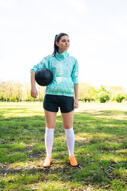 Young female soccer player standing on field holding ball