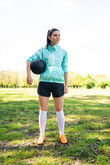 ボールを保持しているフィールドに立っている若い女性のサッカー選手