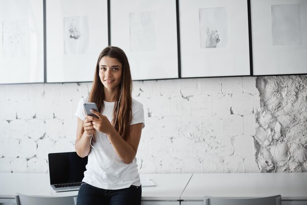 彼女のチームと通信するためにスマートフォンとイヤホンを使用してリモートで作業している若い女性のソフトウェア開発者