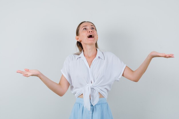 Young female spreading arms, looking up in blouse and skirt and looking merry