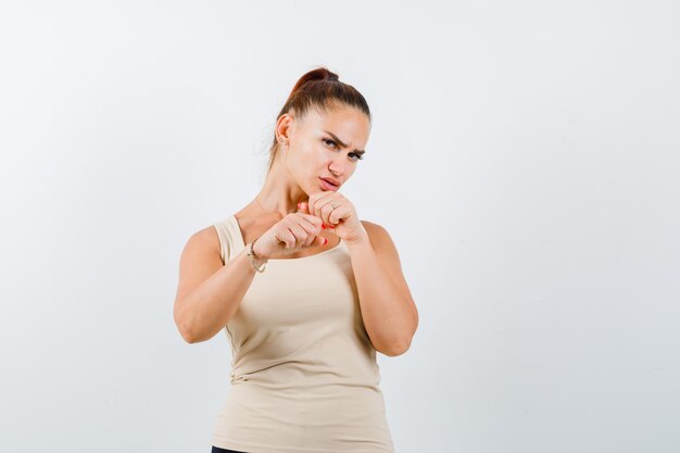 Young female standing in fight pose in beige tank top and looking confident , front view.