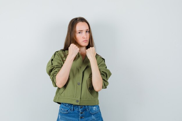 Young female standing in fight pose in jacket, shorts and looking confident. front view.