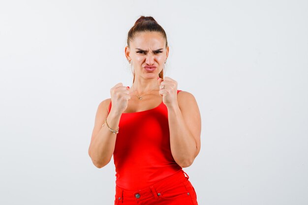 Young female standing in fight pose in red tank top, pants and looking spiteful. front view.