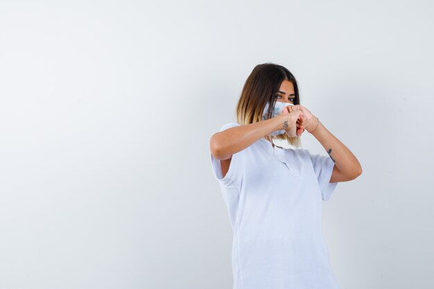 Young female standing in fight pose in t-shirt, mask and looking confident , front view.