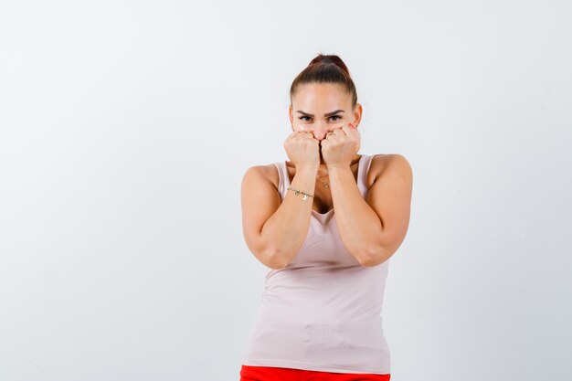 Young female standing in scared pose in white tank top, pants and looking frightened. front view.