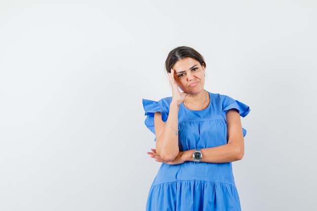 Young female standing in thinking pose in blue dress and looking gloomy