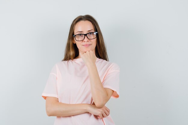 Young female standing in thinking pose in pink t-shirt and looking sensible , front view.