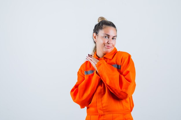 Young female standing with combining hands in worker uniform and looking beloved , front view.