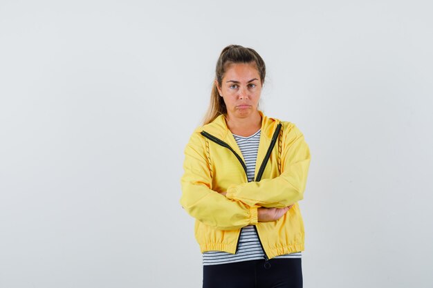 Young female standing with crossed arms in jacket, t-shirt and looking pensive. front view.