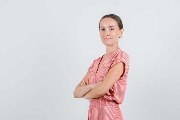 Young female standing with crossed arms in striped dress and looking positive. front view.