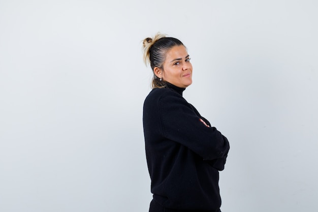 Young female standing with crossed arms in turtleneck sweater and looking confident , front view.