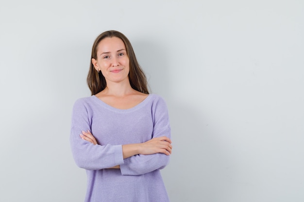 Young female standing with crossed arms while smiling in lilac blouse and looking satisfied 