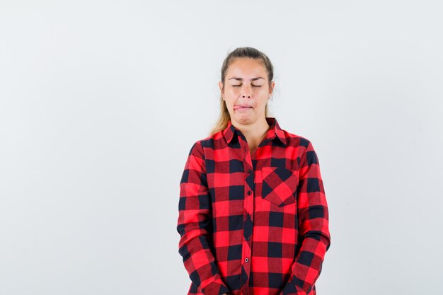 Young female sticking out tongue in checked shirt and looking dreamy , front view.