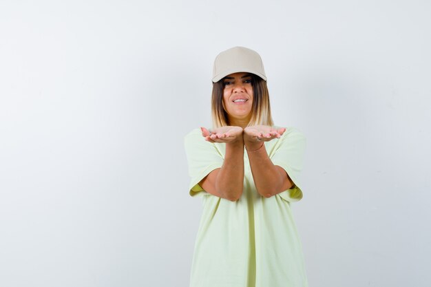 젊은 여성 스트레칭 t- 셔츠, 모자와 귀여운 찾고 손을 cupped. 전면보기.