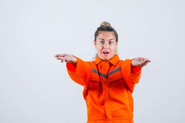 Young female stretching out her hands in worker uniform and looking concentrated , front view.